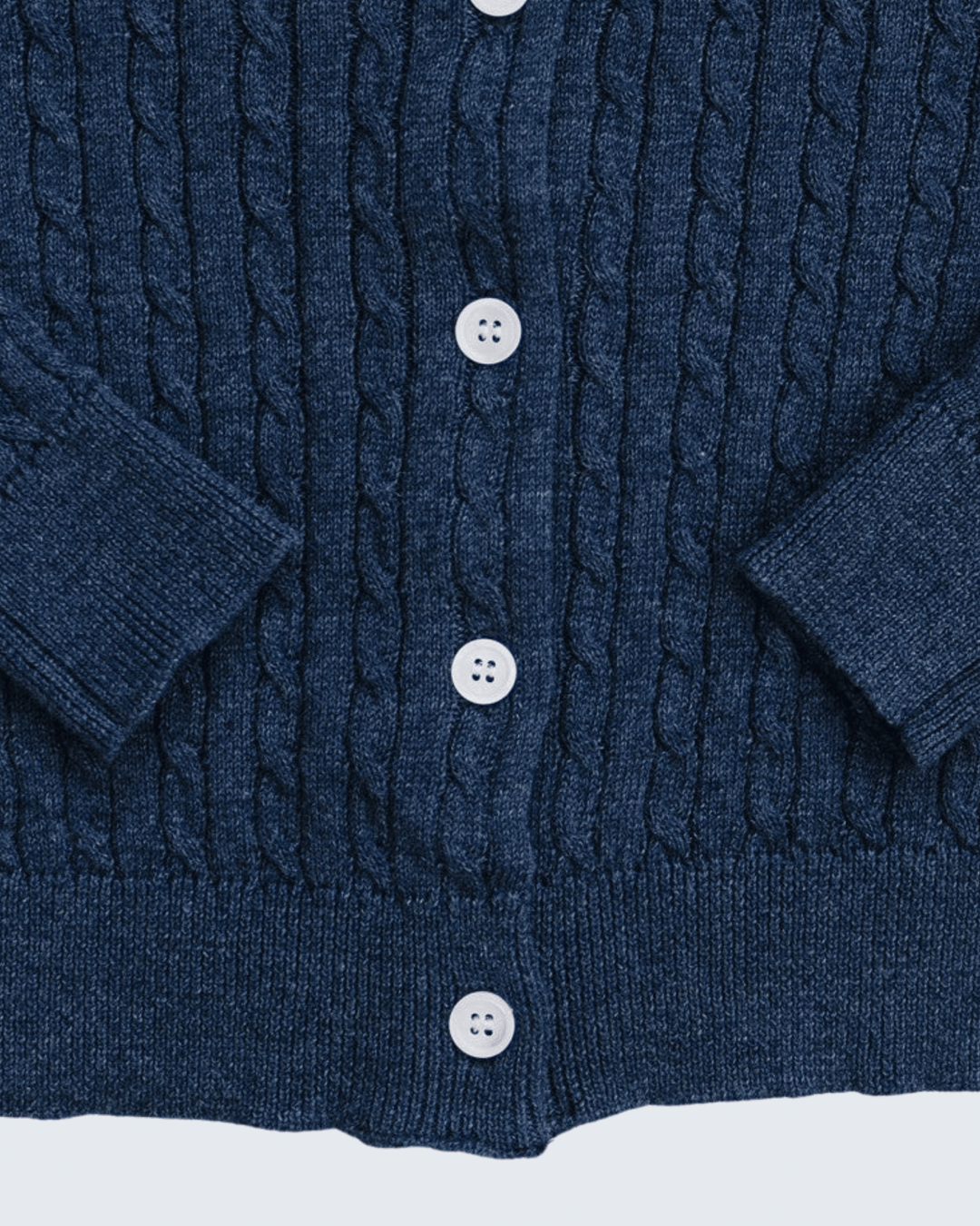 Close-up of a navy blue cable-knit cardigan sweater showing the front button closure with white buttons.