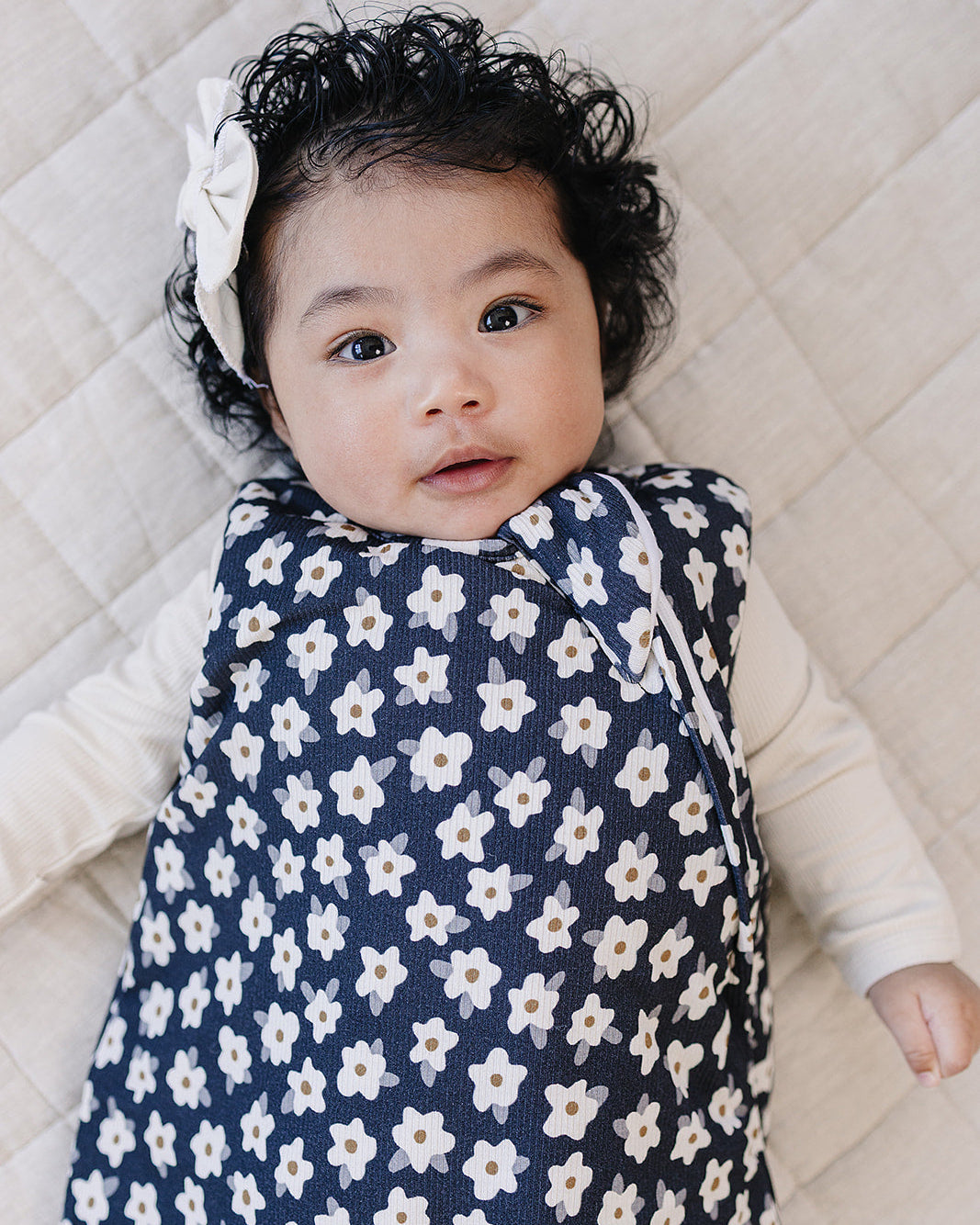 Baby wrapped in a floral sleep sack on a quilted surface