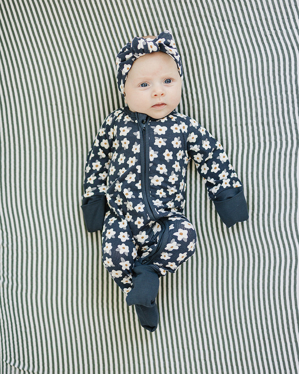 Baby in a floral onesie and headband lying on a striped fabric background