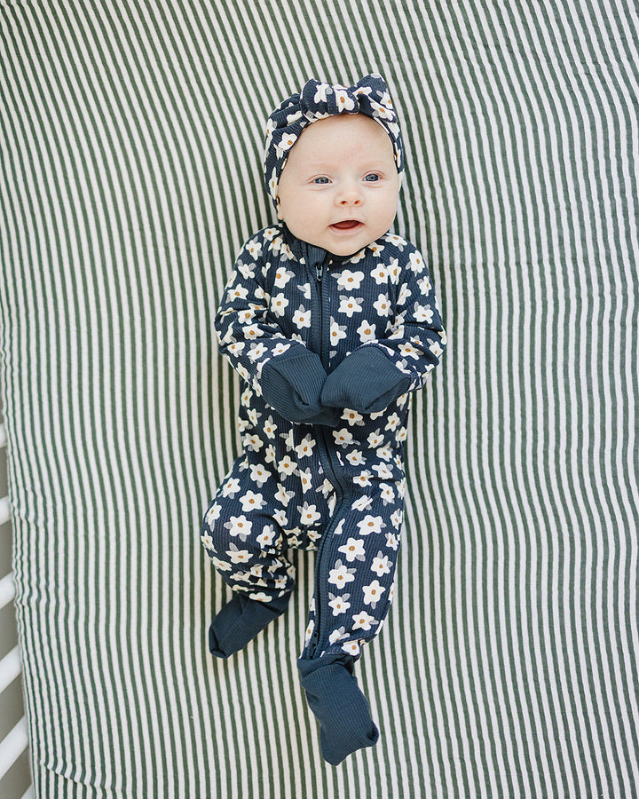 Baby in a floral onesie and navy hat lying on a striped fabric background