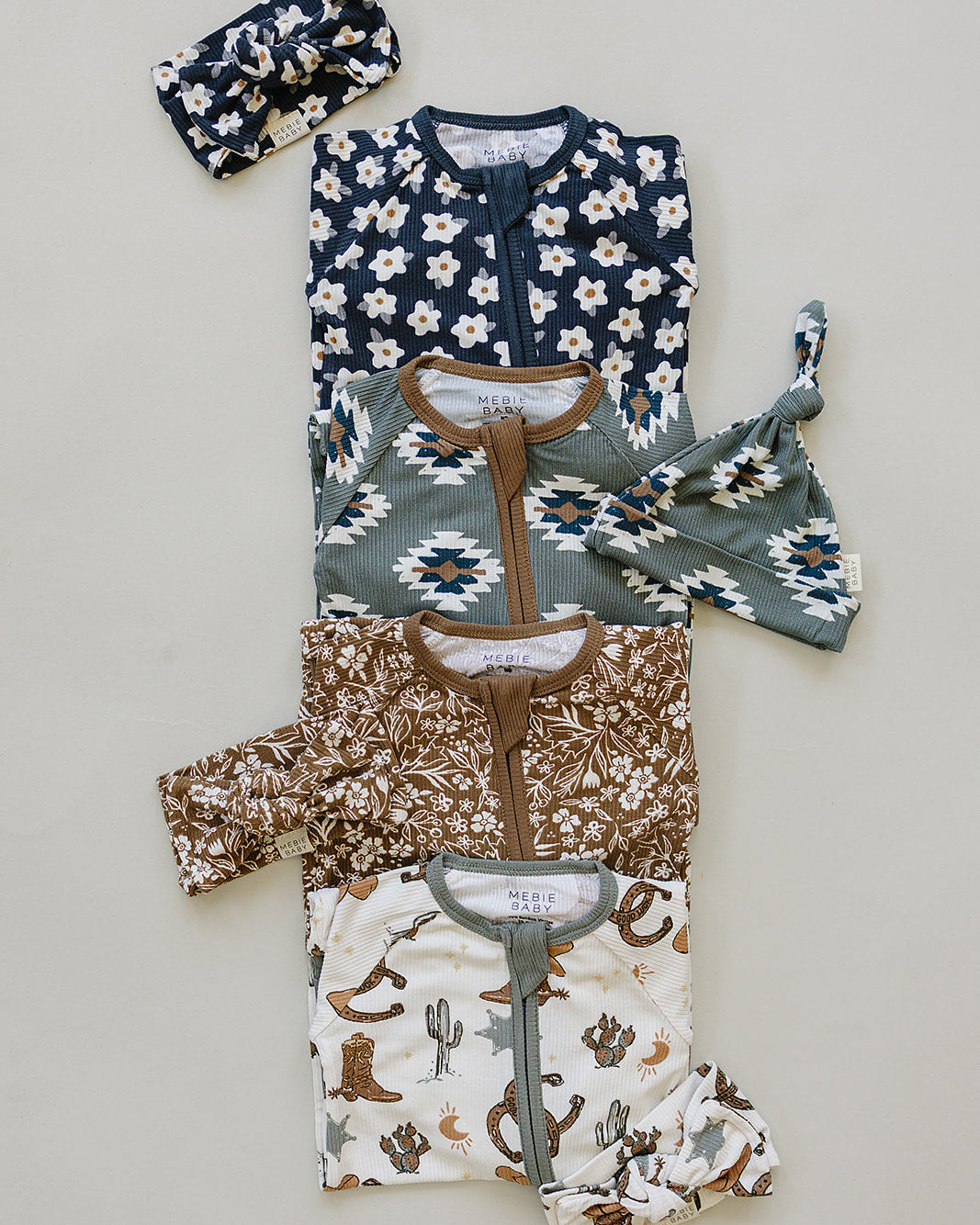 Set of baby rompers with floral, cowboy, and patterned designs on a light gray background.
