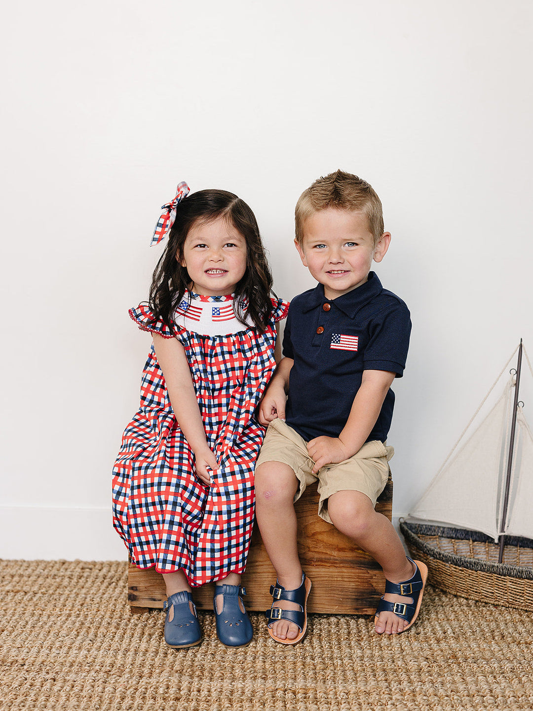 Two children sitting on a wooden block with a sailboat model in the background.