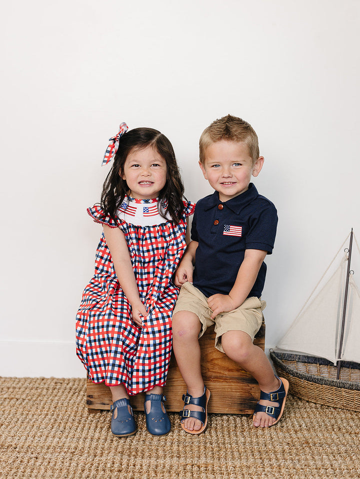 Two children sitting on a wooden block with a sailboat model in the background.