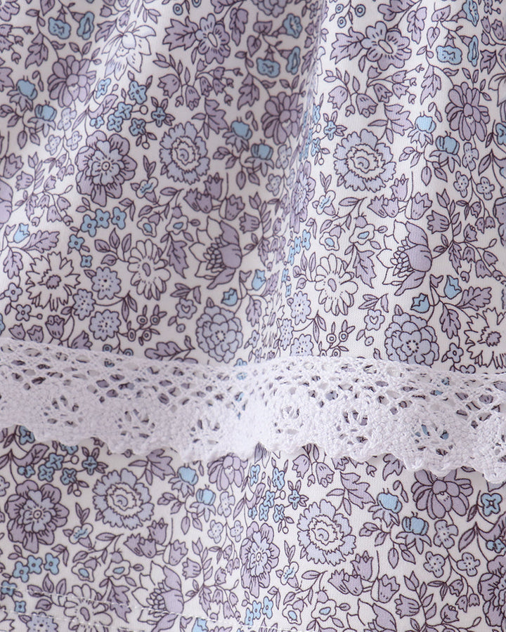 Close-up of a floral fabric with a lavender and light blue print on a white background, featuring a decorative white lace trim.