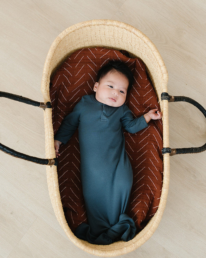 Baby in a woven crib with a textured brown interior on a beige floor.