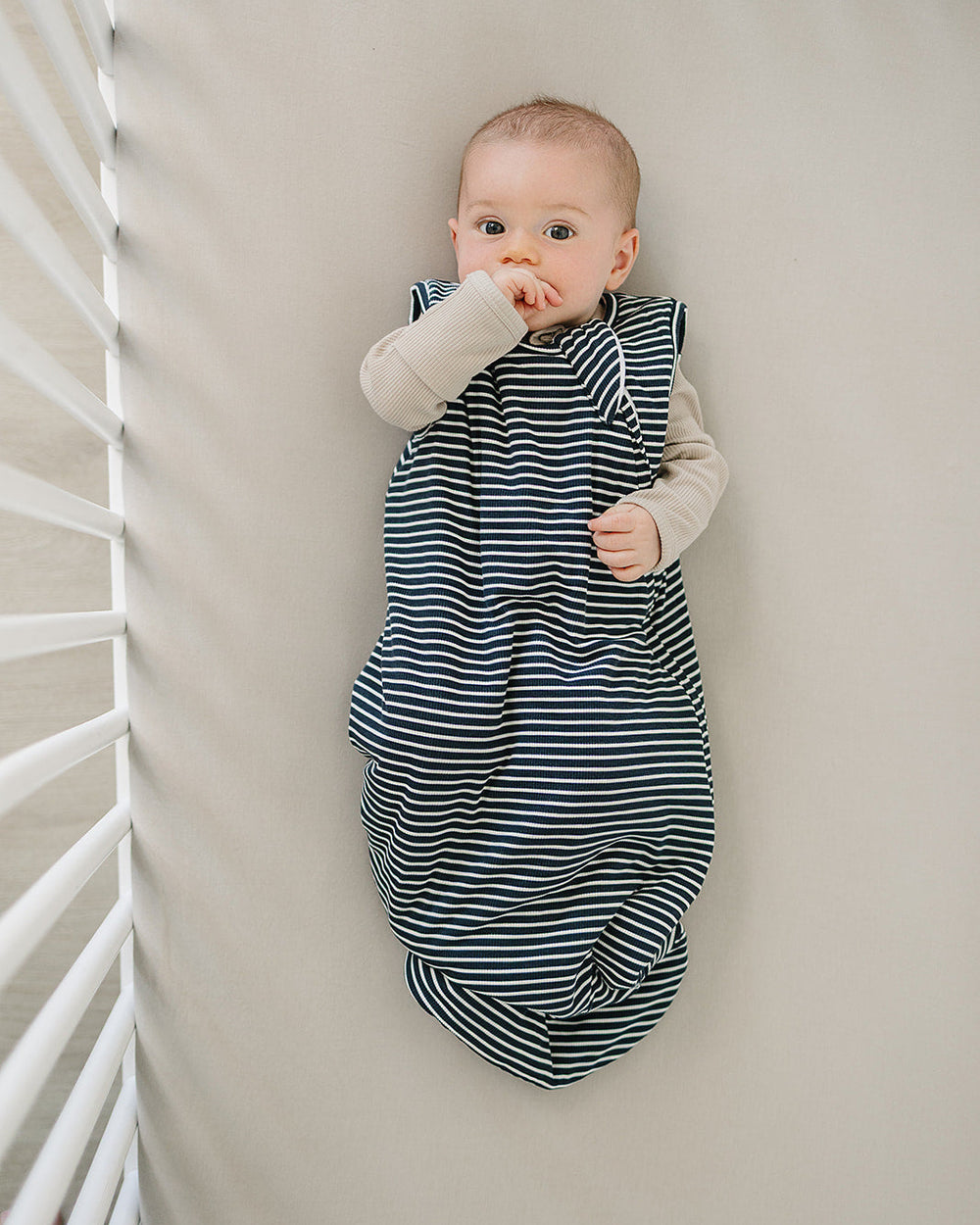 Baby in a striped sleep sack lying on a white floor.