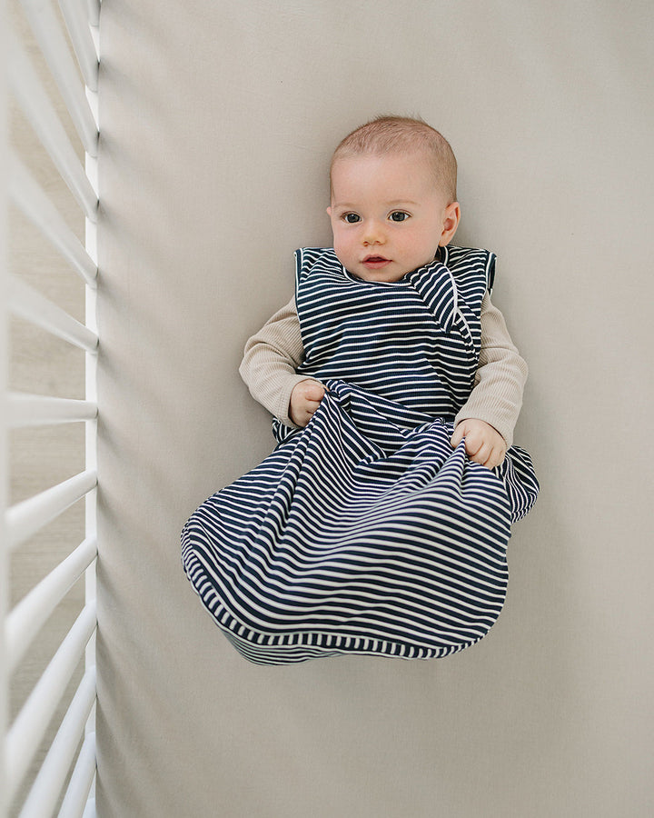 Baby wearing a striped sleep sack lying on a white surface