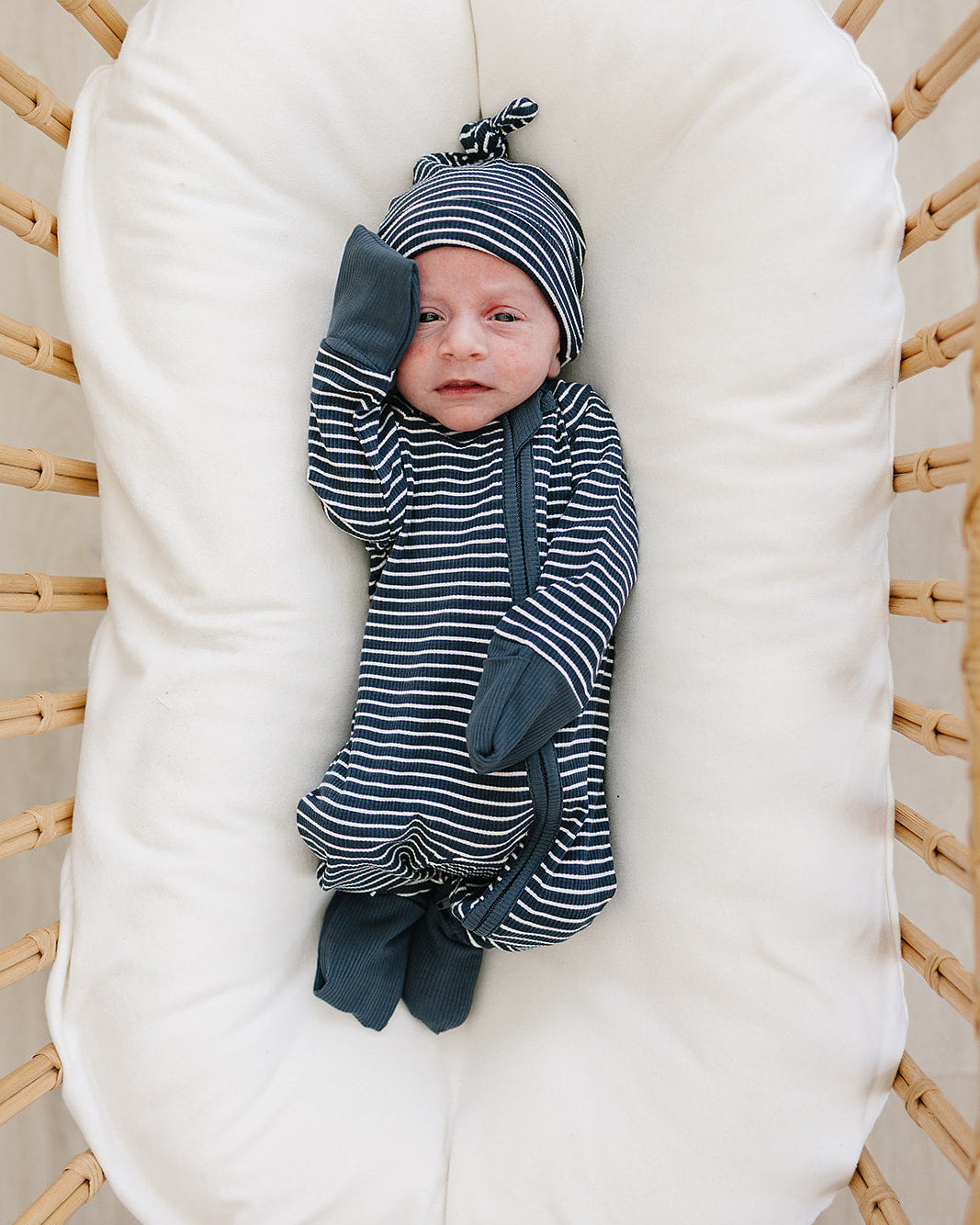Baby wrapped in striped clothing lying on a white cushion in a wooden crib