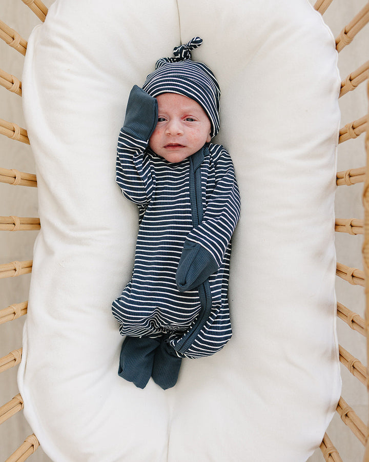 Baby wrapped in striped clothing lying on a white cushion in a wooden crib