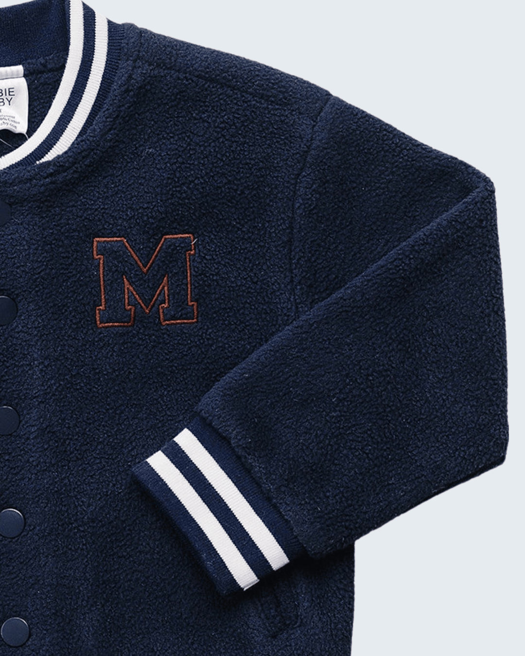 Close-up of a navy blue fleece varsity-style jacket with white striped ribbed collar and cuffs, a large outlined &