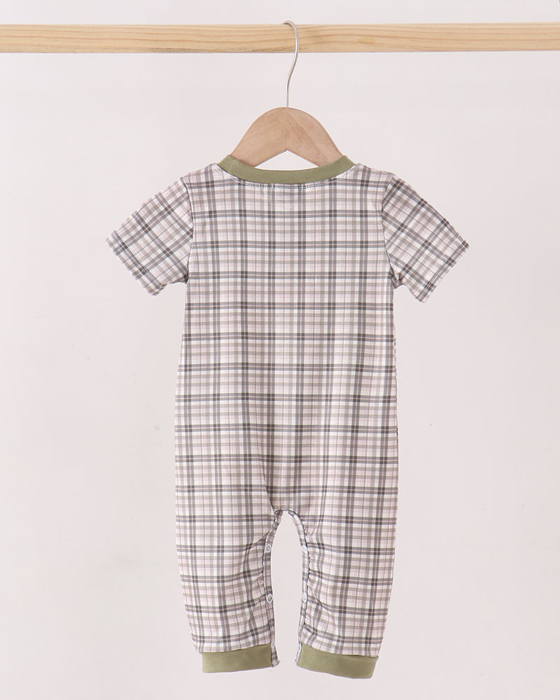 A baby short-sleeve one-piece romper with a brown and beige plaid pattern and sage green trim, hanging on a wooden hanger from a light wood bar against a plain off-white background.