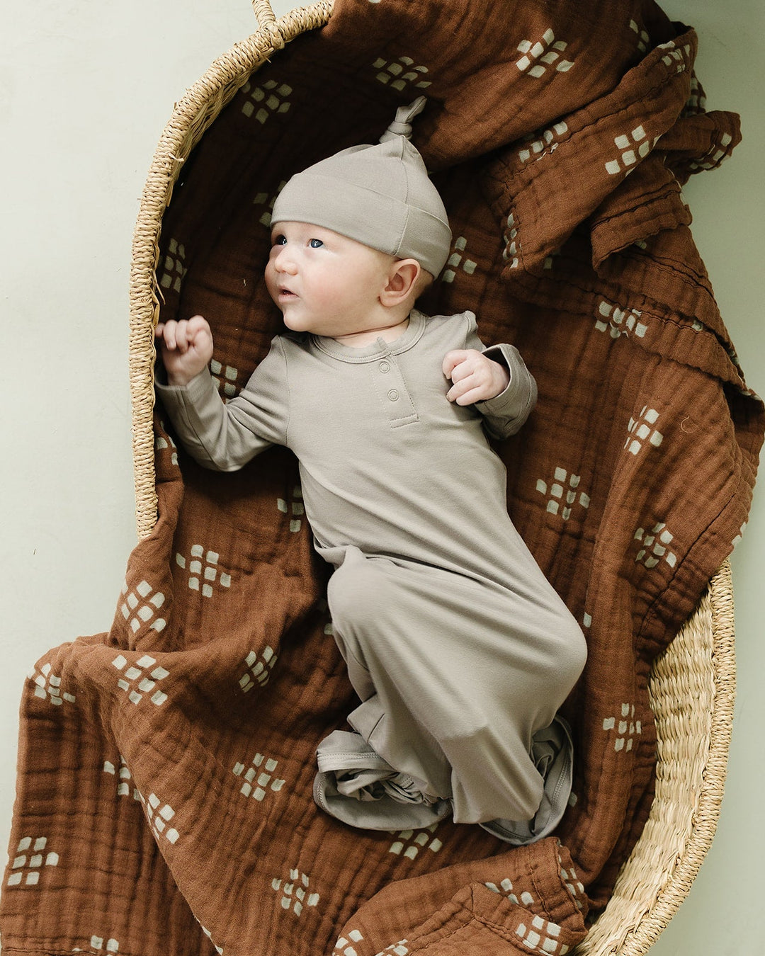 Baby wearing oatmeal bamboo knot hat with swaddle wrap in a woven basket