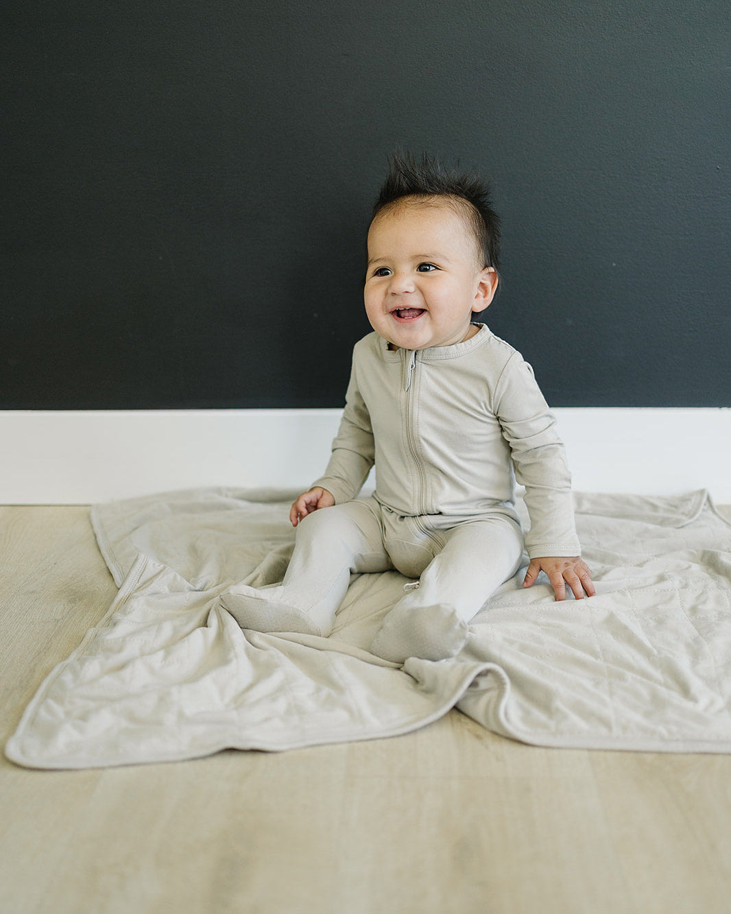 Baby sitting on a beige blanket against a dark gray wall