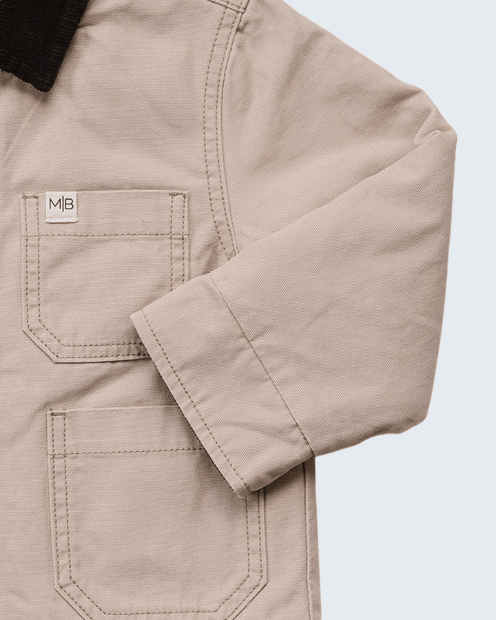 Close-up of a beige kids barn jacket with a chest pocket featuring a small &