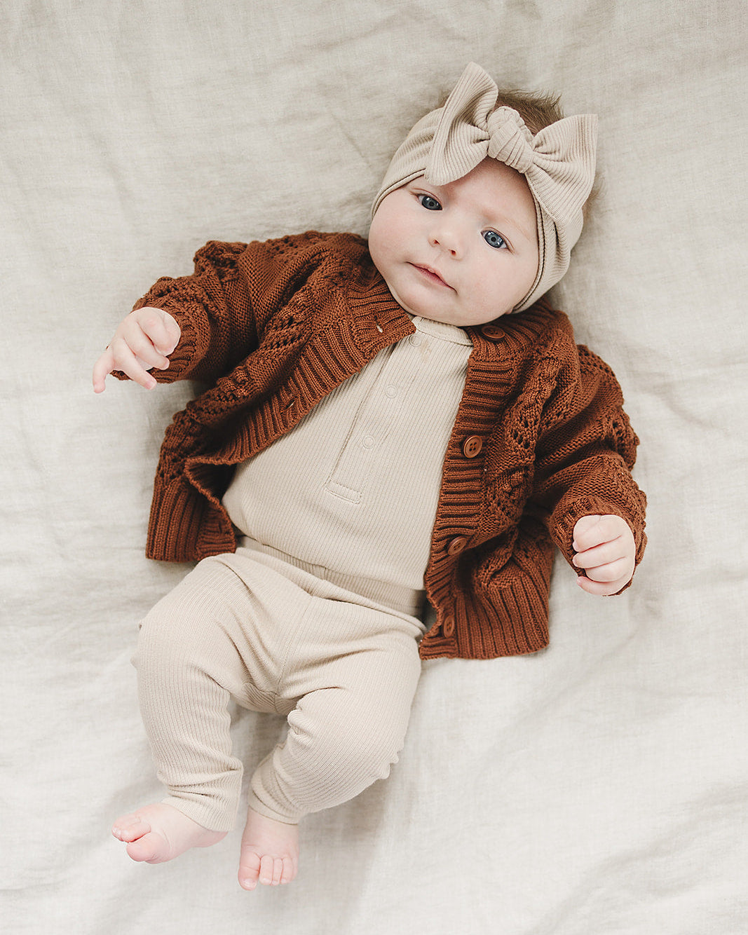Baby wearing a brown cardigan and beige outfit with a matching headband on a light background