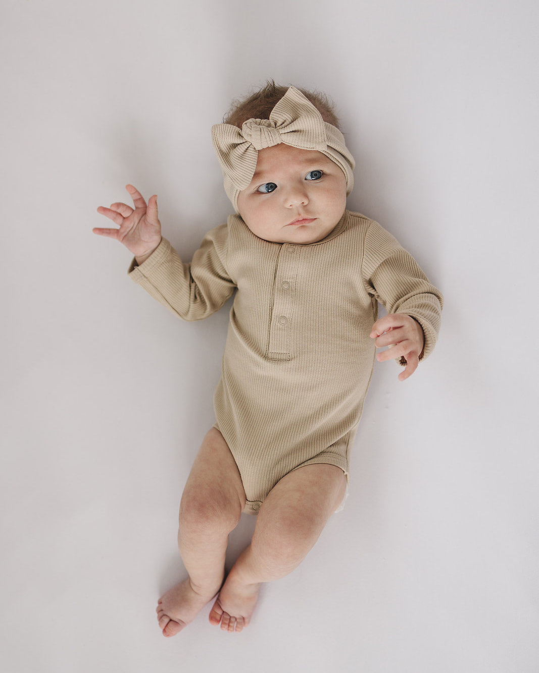 Baby wearing a beige onesie and headband on a light gray background