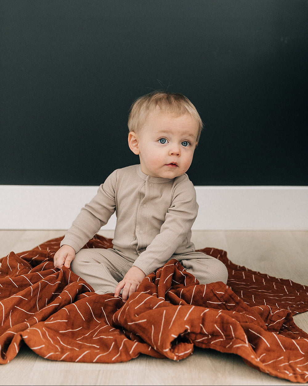 Beige long-sleeve snap romper with button front and footed legs on baby
