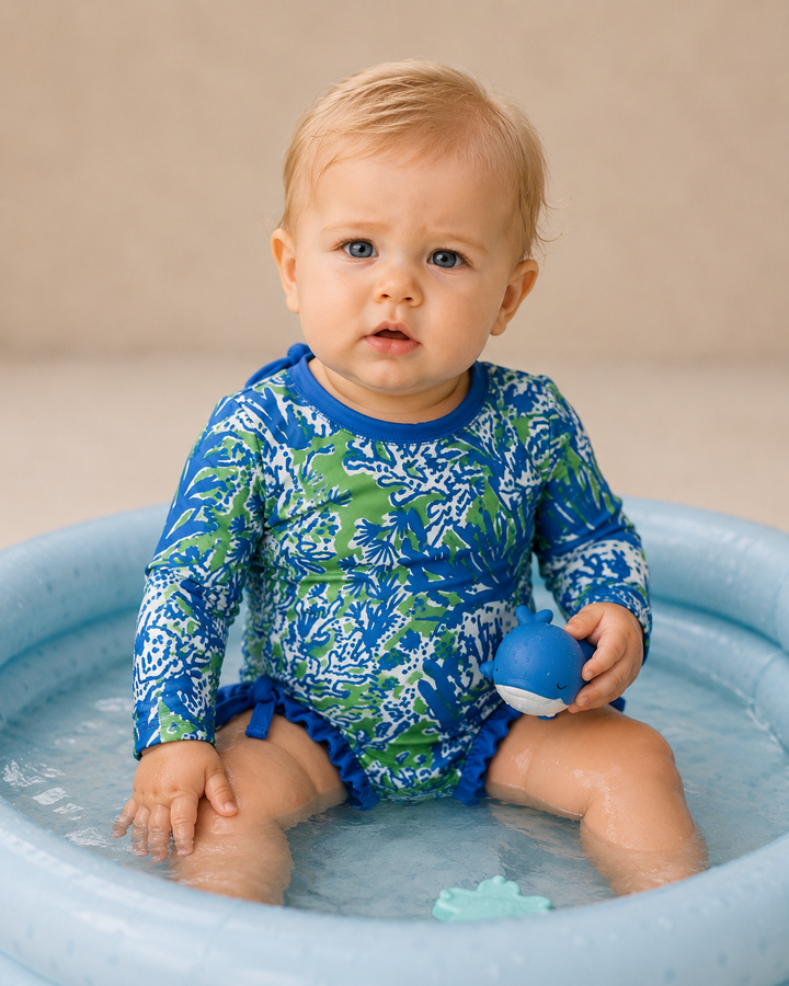 Baby in a blue and green swimsuit sitting in a small pool.