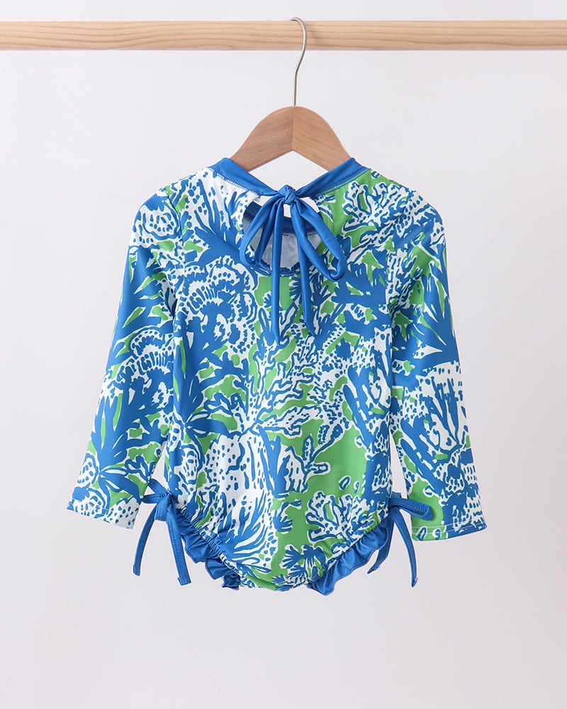 Blue and green patterned rashguard on a wooden hanger against a white background