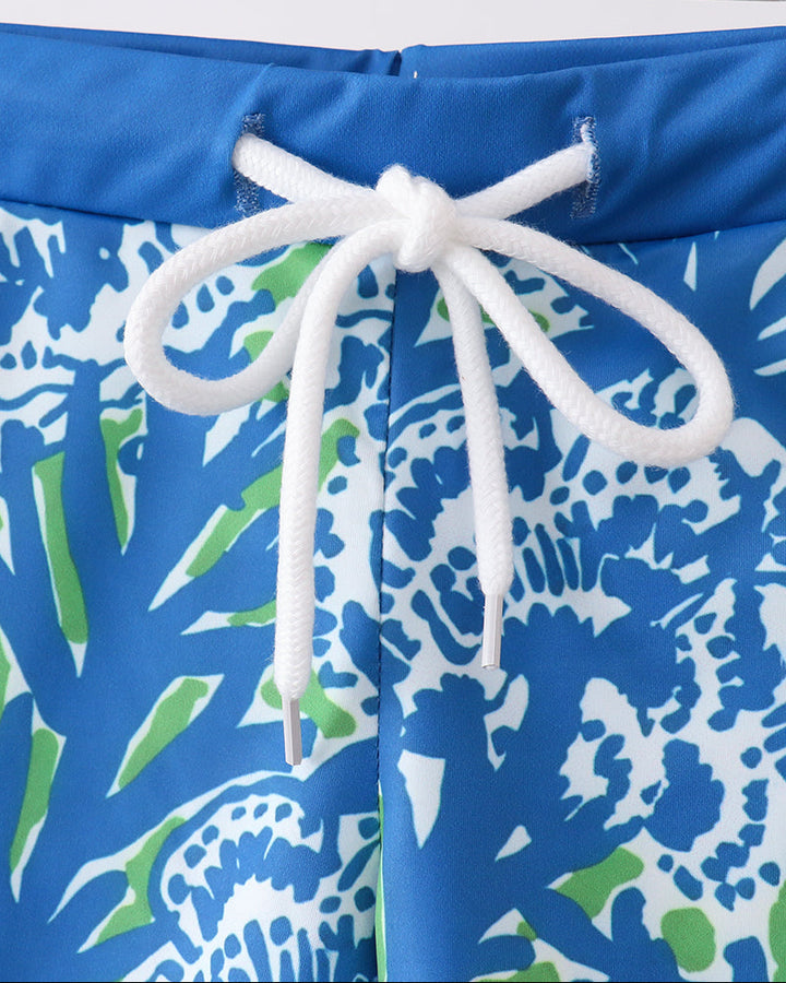 Blue swim shorts with white drawstring on a wooden hanger against a white background