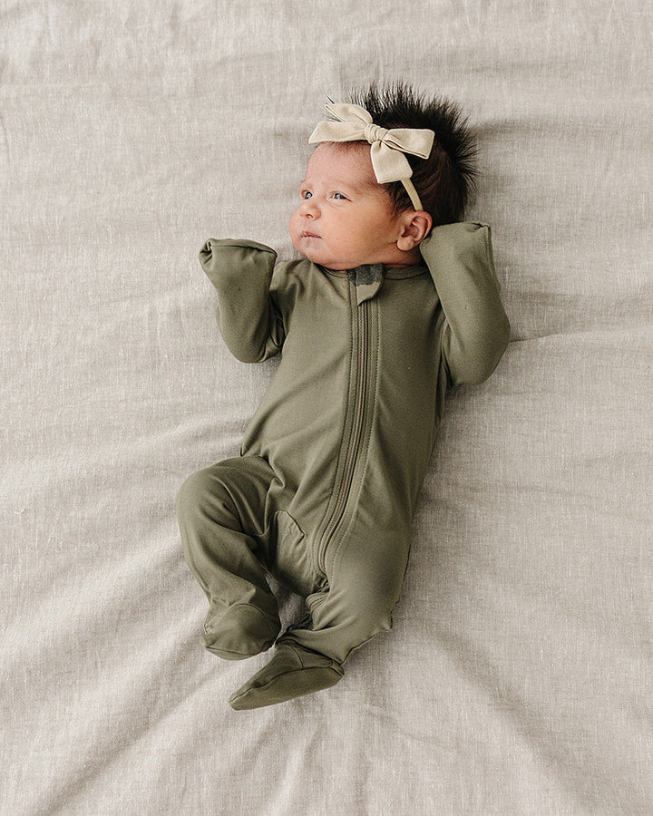 Newborn baby in a green onesie with a headband lying on a textured surface