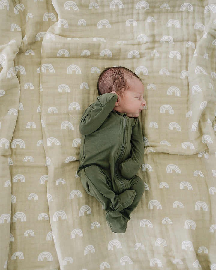 Newborn baby in a green outfit lying on a soft, patterned blanket