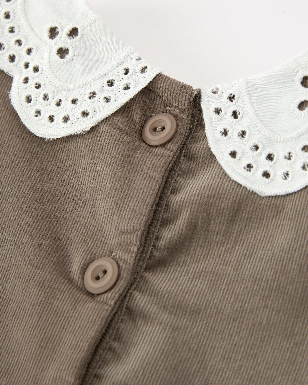 Close-up of a brown corduroy garment with a white eyelet Peter Pan collar and brown buttons.