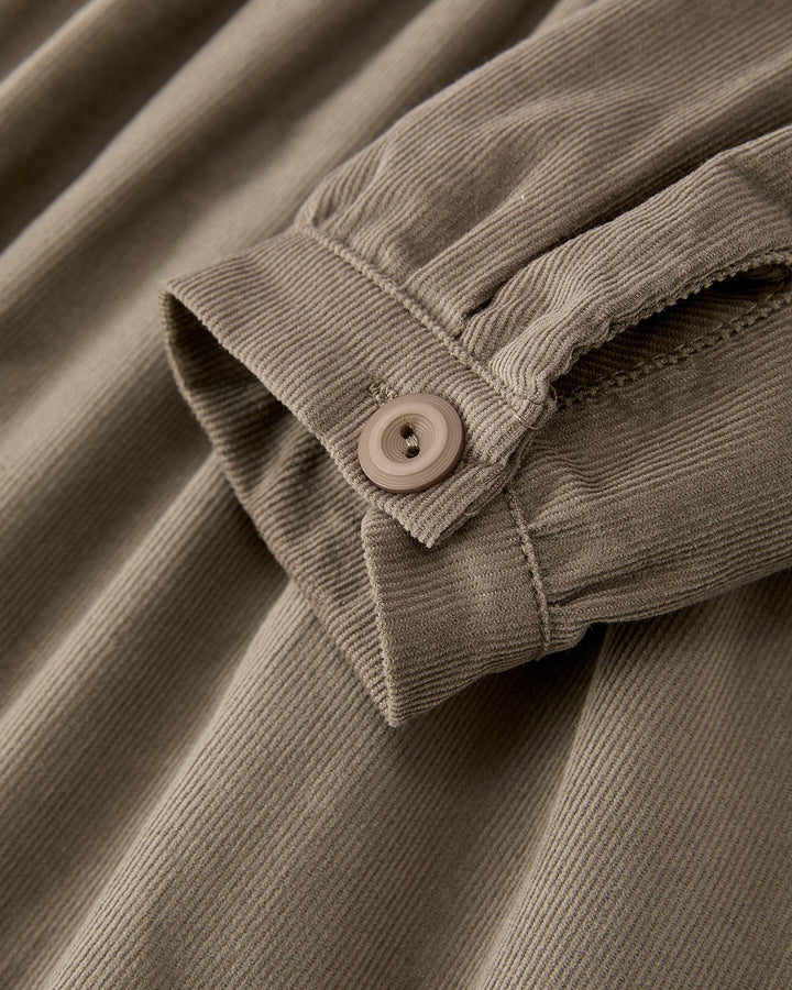 Close-up of a corduroy garment in a warm taupe-beige color, showing the ribbed fabric texture and a matching button on the cuff.