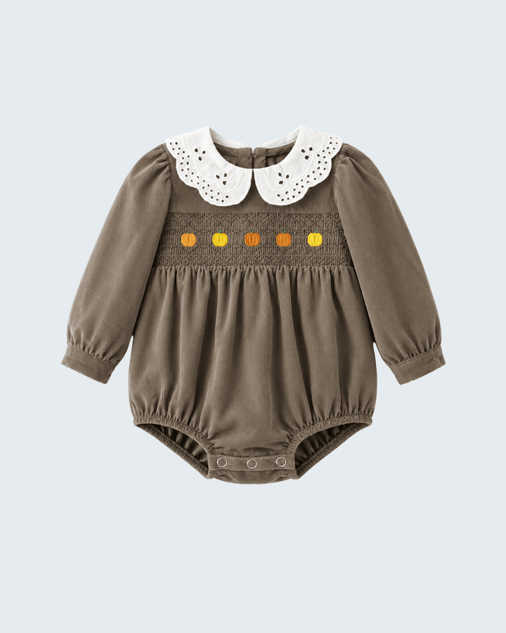 A baby long-sleeve smocked romper in taupe brown, featuring a white eyelet Peter Pan collar and a smocked chest band with orange and yellow embroidered details, shown on a light gray background.