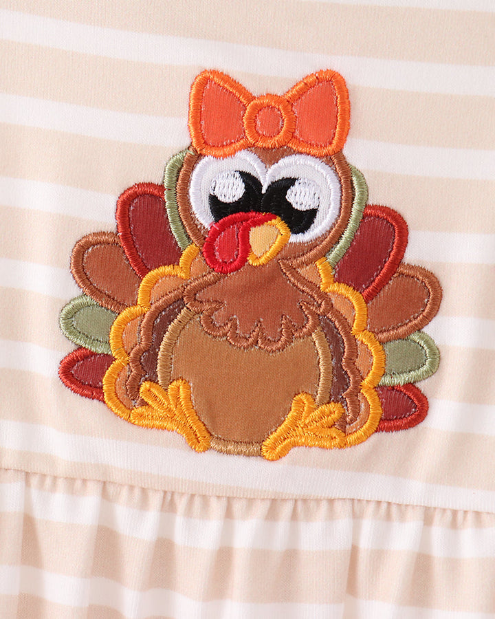 Turkey applique bib with orange bow on striped romper, close-up