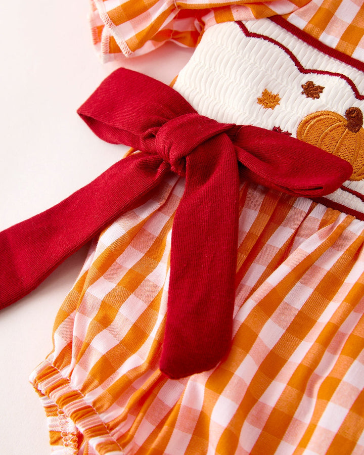 Orange checkered romper with wide red bow tie at waist and gathered ruffled hem