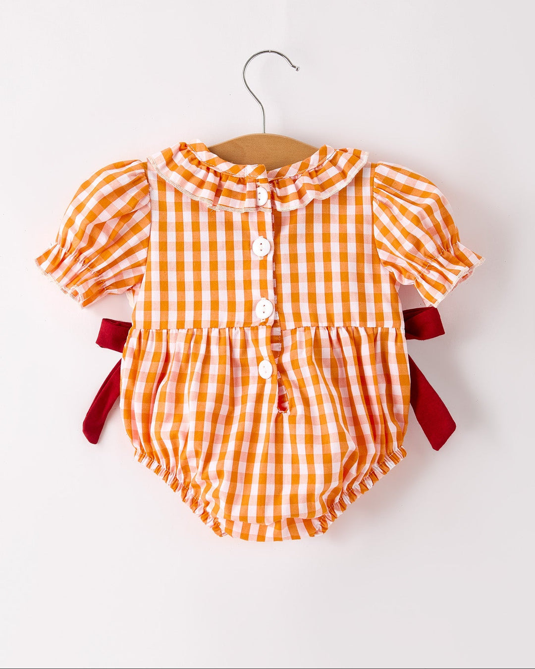 Orange checkered baby romper with short puff sleeves, button front, and red bow accents