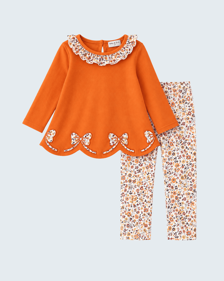 Orange long-sleeve top with lace-like floral collar and scalloped hem; floral pants