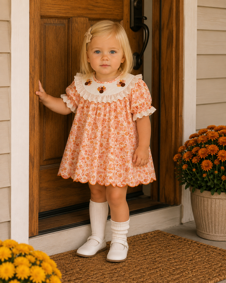 Toddler wearing an orange floral lace dress with white ruffled yoke and puff sleeves