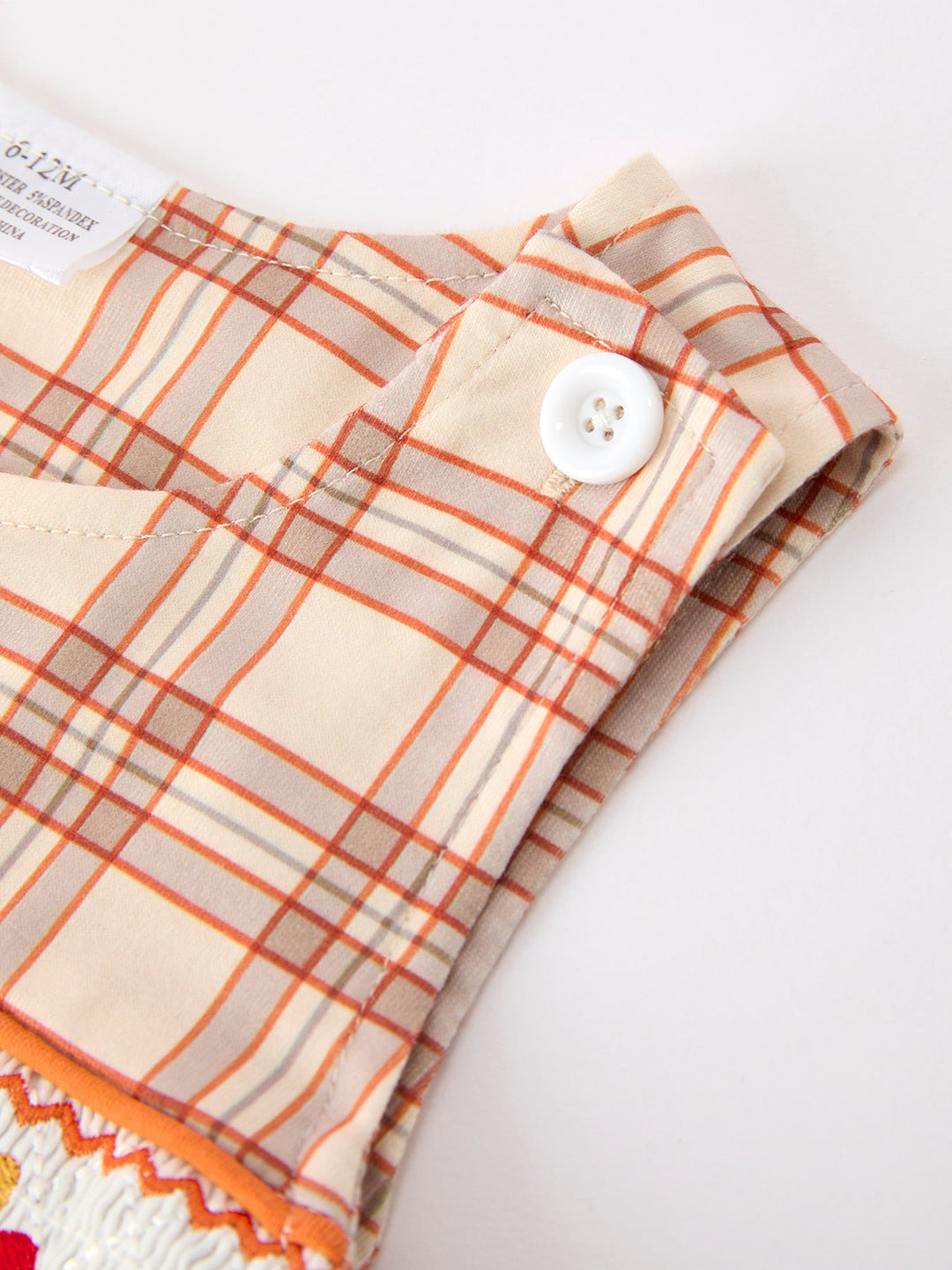 Close-up of orange plaid baby Jon Jon with round white button on bib
