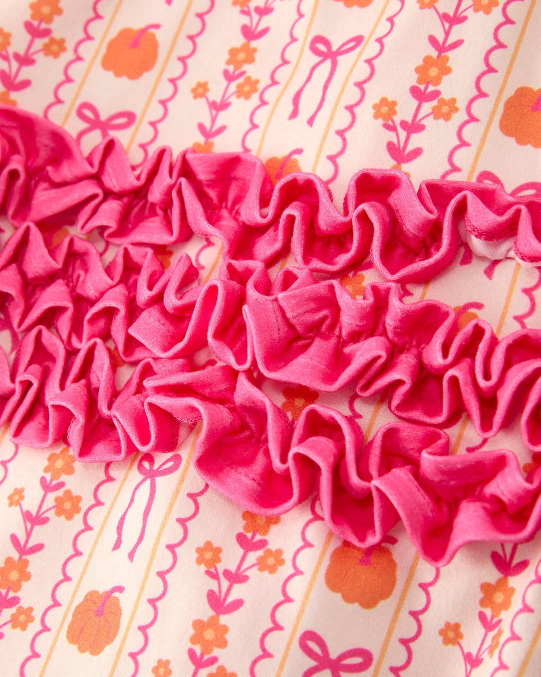 Close-up of pink ruffle detail on patterned baby sleeper fabric