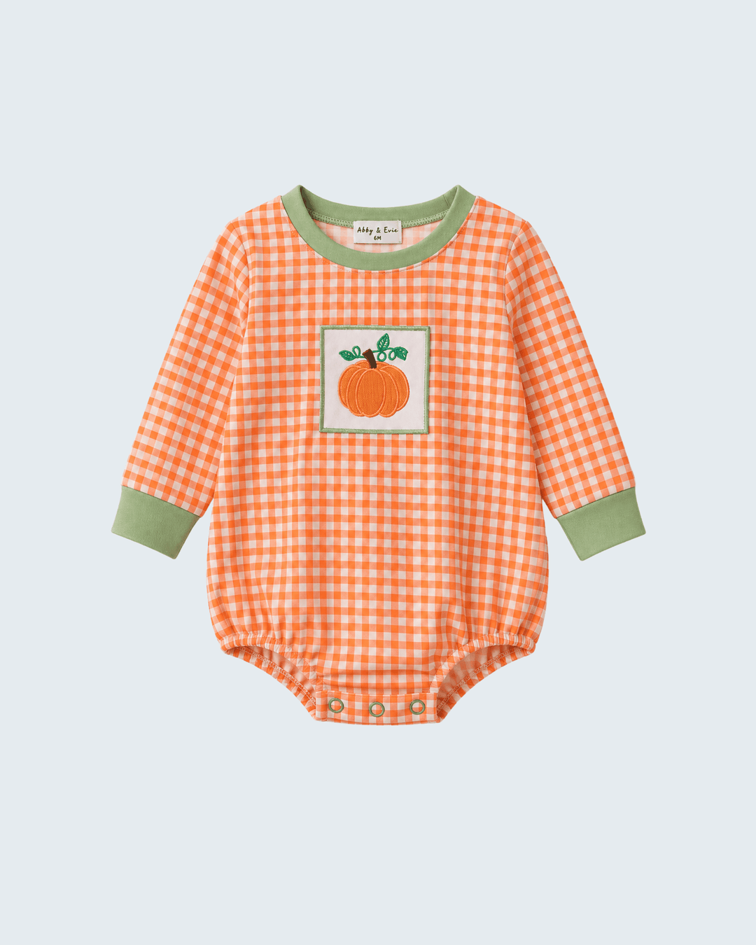 A baby long-sleeve bodysuit in orange and white gingham with sage green trim on the collar and cuffs, featuring a pumpkin patch graphic on the chest.