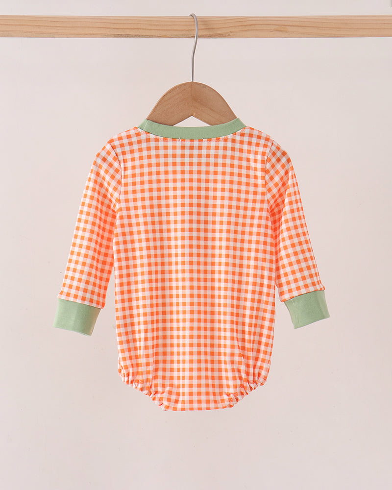 A baby long-sleeve romper with an orange and white gingham check pattern, featuring sage green trim on the collar and cuffs, hanging on a wooden hanger.