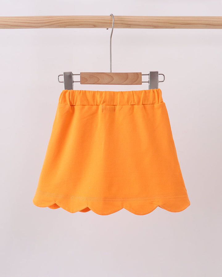 Orange scallop-hem skort hanging on a wooden hanger with waistband tie