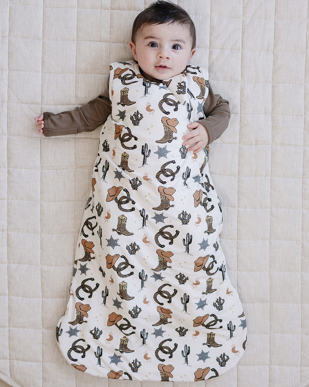 Baby lying on a quilted surface wearing a patterned baby wrap with cowboy boots and stars.