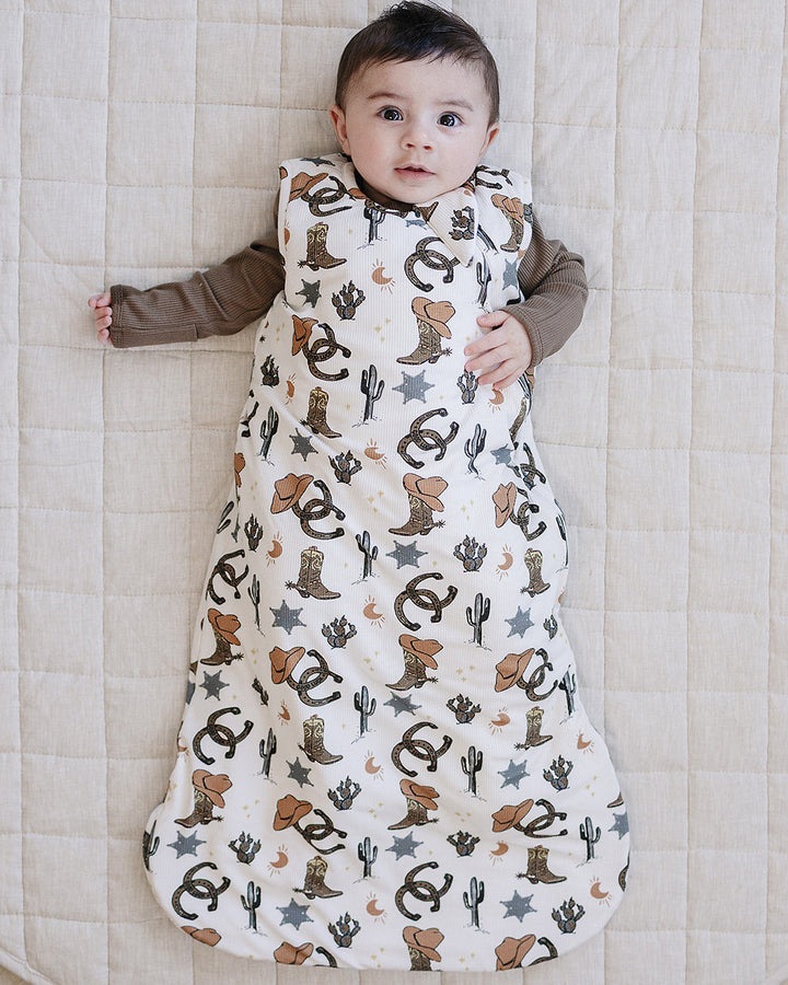 Baby lying on a quilted surface wearing a patterned baby wrap with cowboy boots and stars.