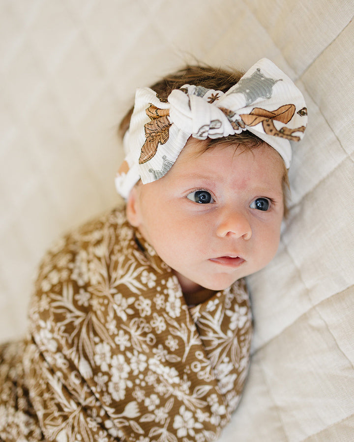 Baby wearing knot-front head wrap with cowboy print, ribbed beige fabric