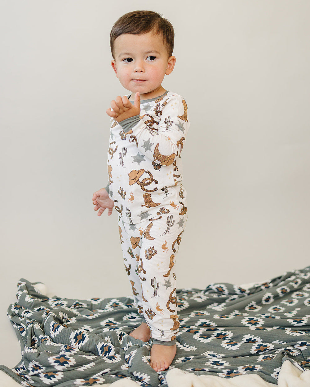 Child wearing a patterned pajamas standing on a blanket with a plain background