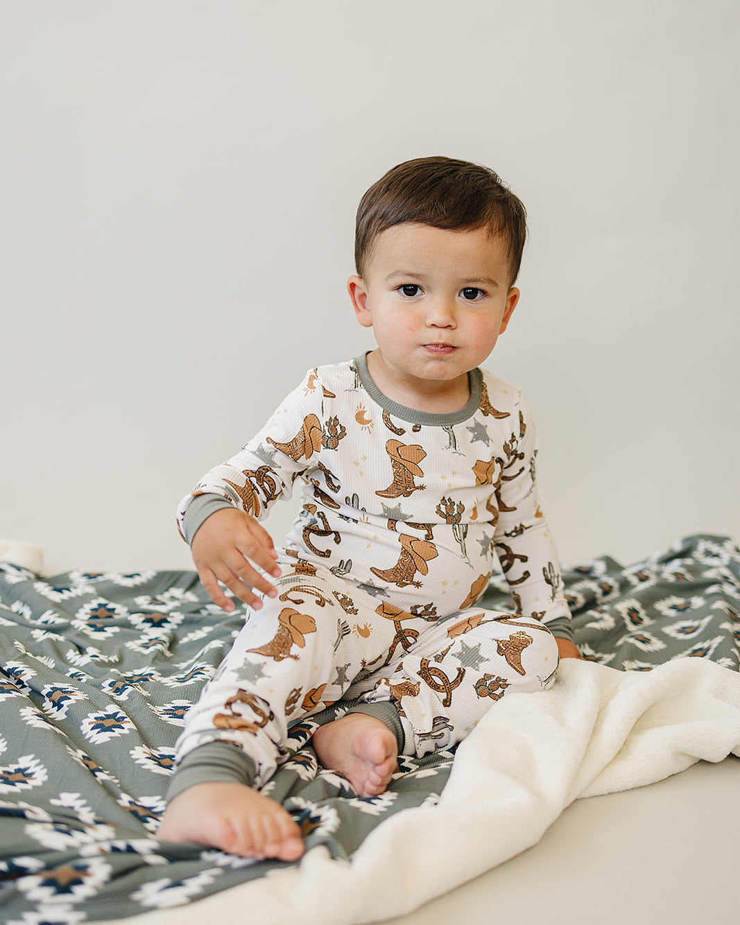 Baby wearing a o pajamas with western pattern sitting on a blanket
