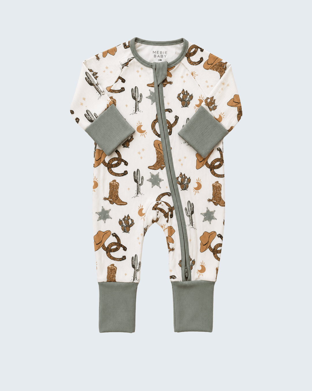 A baby long-sleeve footless one-piece sleeper with a western print, featuring brown cowboy boots, hats, cacti, and stars on an off-white background, with sage green cuffs, collar, and zipper trim.