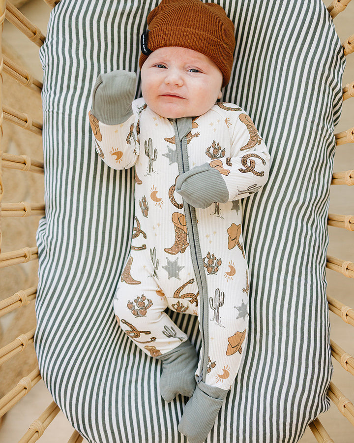 Baby in a striped baby bouncer wearing a cowboy-themed outfit and brown hat.