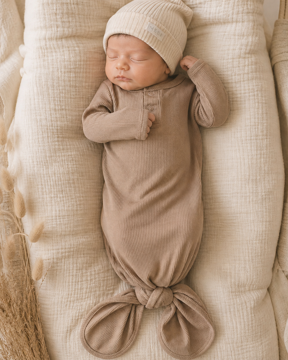 Newborn baby wrapped in a pale pink swaddle and hat, lying on a textured surface.