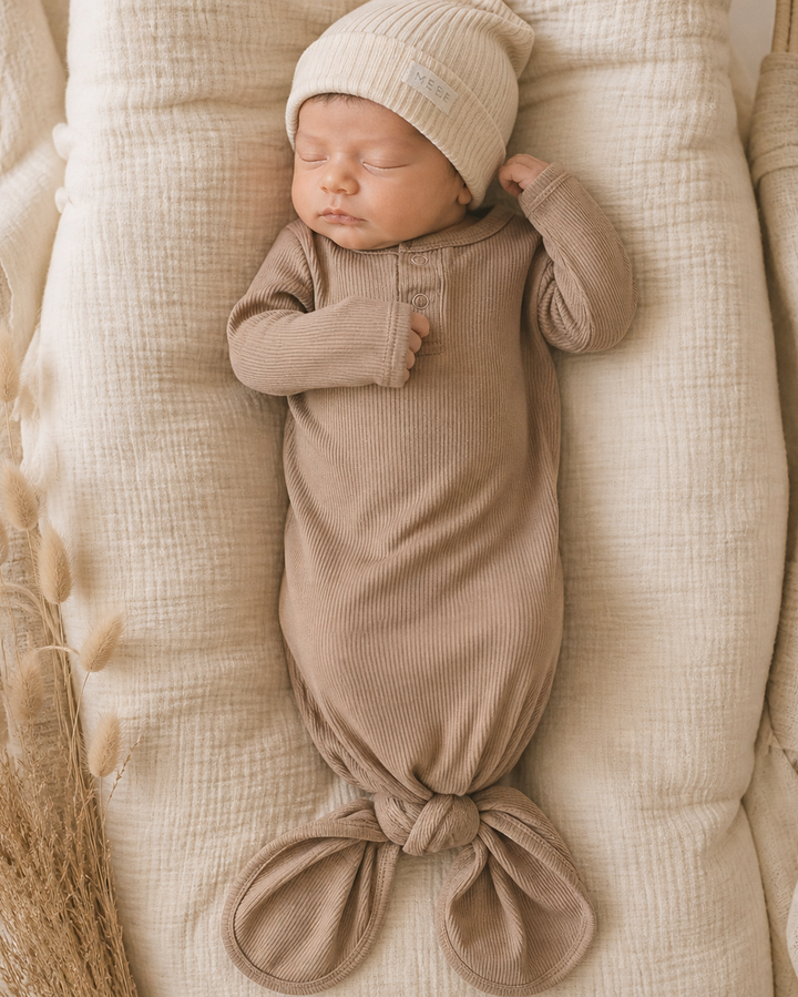 Newborn baby wrapped in a pale pink swaddle and hat, lying on a textured surface.