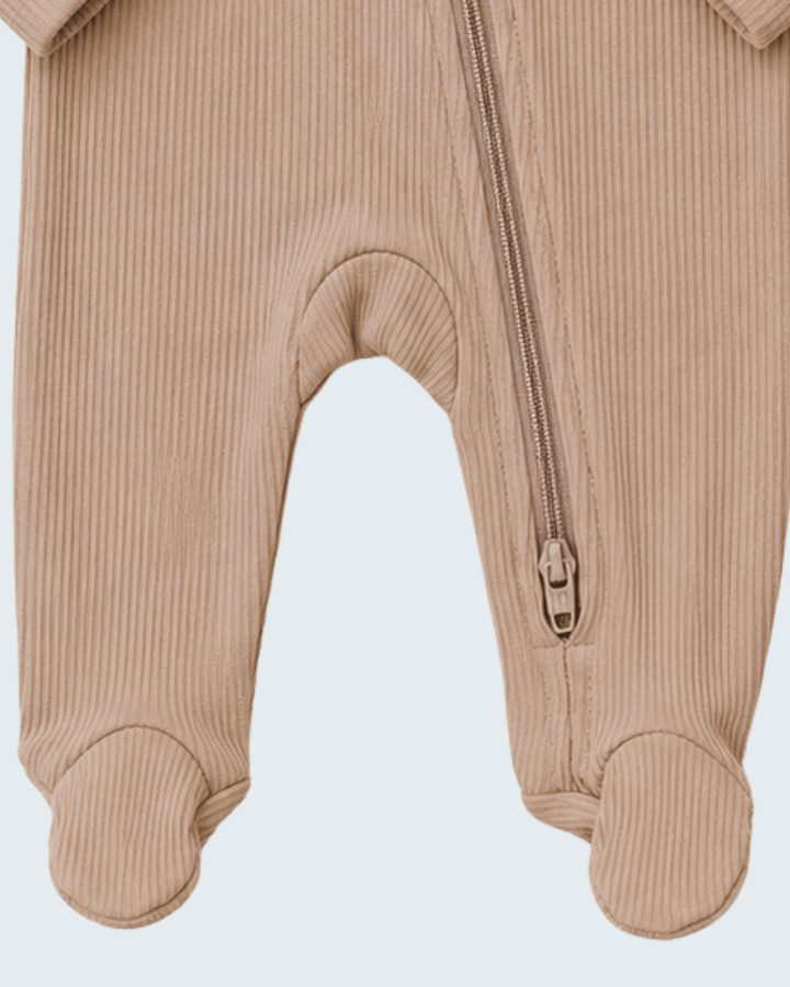 Close-up of a baby footed one-piece outfit in beige ribbed corduroy fabric, showing the front zipper and ankle openings against a light gray background.