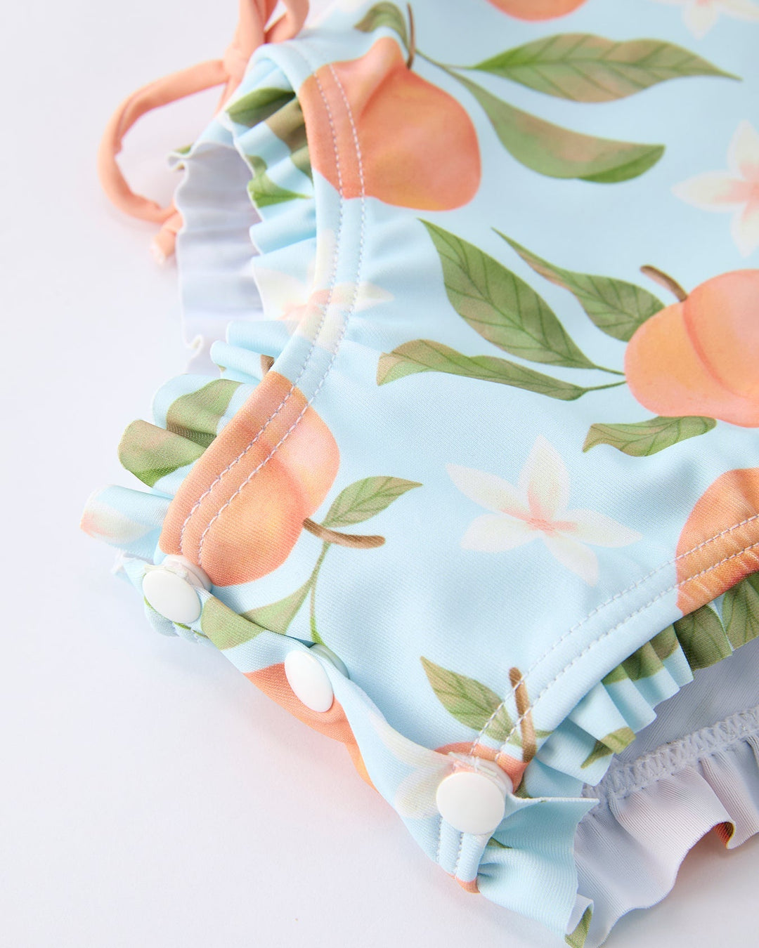 Baby swimsuit with peach and leaf pattern on a light blue background